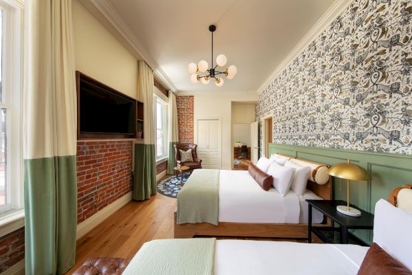 A stylish hotel room with two beds, a wall-mounted TV, brick and patterned walls, a trendy chandelier, and a wooden floor.