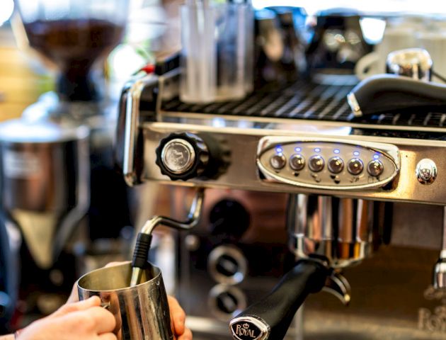 A person is using a coffee machine, frothing milk with a steam wand, likely in a cafe or coffee shop setting.