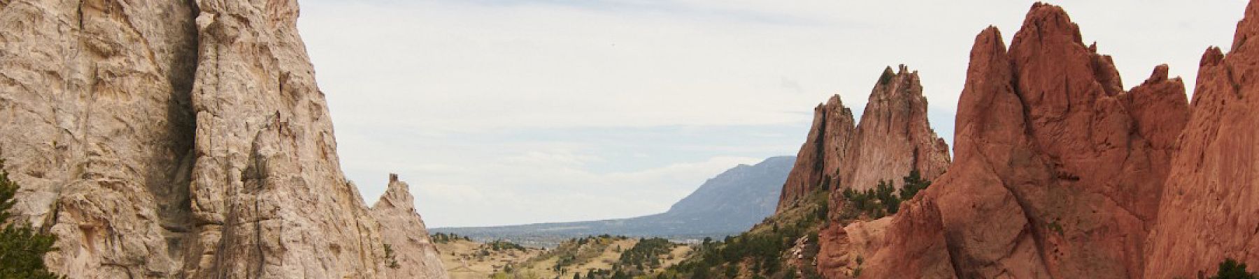 The image shows a scenic landscape with sandstone rock formations, a walking path, some people, and a distant mountain under a partly cloudy sky.