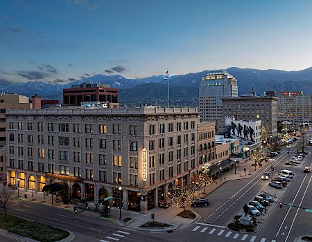 A cityscape at dusk with buildings, a busy street with cars, and mountains in the background. The scene captures the tranquil and vibrant essence of urban life.